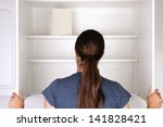 Food Insecurity Concept: Closeup of a woman looking in an empty pantry. Seen from behind there is only one box of food. Horizontal format.