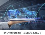 The bulls and bears struggle. Equity market illustration. Close up of hand holding tablet with creative hologram and graph on blurry office interior background. Double exposure