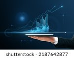Close up of businessman hand pointing at tablet with abstract glowing polygonal business graph hologram with growing arrow on blurry background. Financial growth, market and trade concept