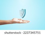 Small photo of Close up of female hand holding creative antivirus shield icon on light blue background. Secure phone usage, protection and web safety concept