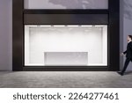 Man walking by evening empty shop window with podium inside for your product presentation on glowing white background in modern building area outdoors, mock up