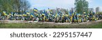 Small photo of Kyiv city 2023. Huge big yellow fabric wreath decor style many young man sad male mortality grief spirit sorrow green tree bush yard park outdoor nature town holy history home view blue sky text space