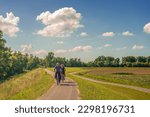 Small photo of HANK, THE NETHERLANDS - JULY 3 2016: An unidentified man and woman cycle one behind the other on a winding cycle path through a polder area in the province of North Brabant. It's a sunny summer day.