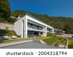 Modern house of two apartments with a beautiful garden directly on Lake Ceresio. Sunny day with blue sky. Minimalist and linear architecture. Panoramic view in background of green hills during summer.