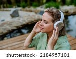 Rlaxed woman wearing headphones listening to music sitting on a pier by natureal lake in summer