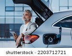 Businessman using tablet while charging car at electric vehicle charging station, close-up.