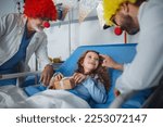 Small photo of Happy doctors with clown red noses celebrating birthday with little girl in hospital room.