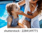 Small photo of Young mother applying sunscreen lotion to her daughter. Safety sunbathing in hot day.