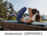 Small photo of Side view of young sporty woman doing bicycle crunches on gym mat in the city.