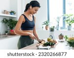 Small photo of Shoot of athletic woman cutting fruits and vegetables to prepare a smoothie while listening to music with earphones in the kitchen at home