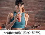 Shot of beautiful sporty woman driking a healthy smoothie while using smartphone in the kitchen.
