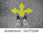 A pair of feet standing on a tarmac road with yellow arrow print pointing in three different directions for the concept of making decision at the crossroad.