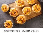 savory puff cups with ham, eggs and Cheddar cheese close-up on a wooden board on the table. Horizontal top view from above