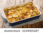 Small photo of Scalloped potatoes, potato casserole with the addition of herbs, onion and garlic in a ceramic baking dish closeup on the table. Horizontal
