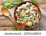 Small photo of Homemade salad of boiled eggs, potatoes, tomatoes, onions and sorrel, spinach with cream dressing close-up in a bowl on a wooden table. Horizontal top view from above