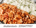 Small photo of Classic Swedish Dish Flygande Jakob made of chicken, cream, chilli sauce, bananas, roasted peanuts and bacon served with rice closeup on the plate on the table. Horizontal