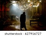 Silhouette of a man in a coat and hat in a dark alley on a rainy night