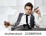Young rich successful man sitting in white leather armchair with cigar and glass of whiskey. Fashion style portrait in modern interior.