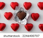 Love and relationship concept - close up of wrapped and unwrapped heart shape chocolate candies in red foil over white background