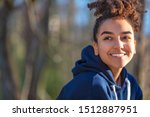 Outdoor portrait of beautiful happy mixed race biracial African American girl teenager female young woman smiling with perfect teeth wearing a blue hoodie
