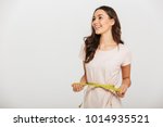 Portrait of a happy young asian woman holding measuring tape around her waist and looking away at copy space over white background