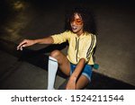 Image of hipster african american girl in streetwear smiling and riding on skateboard at night outdoors