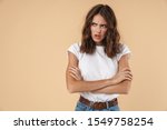 Portrait of a lovely angry young girl wearing casual clothing standing isolated over beige background, arms folded