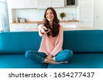 Image of a positive smiling optimistic young woman sit indoors at home watch tv holding remote control on sofa.