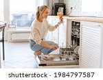 Smiling young white woman putting dishes in the dishwasher at home