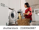 Young hispanic brunette woman putting clothes at washing machine while doing laundry at home
