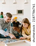 Small photo of Adopted african little girl solving puzzles with father and sister in living room at home. Adoption concept.
