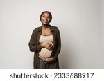 Small photo of African pregnant happyyoung woman standing and holding her belly looking in camera over isolated brown background