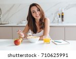 Smiling healthy woman eating corn flakes cereal while sitting and having breakfast at the kitchen table
