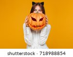 Image of happy young woman dressed in crazy cat halloween costume over yellow background with pumpkin.