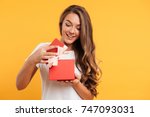 Portrait of a happy smiling girl opening a gift box isolated over yellow background