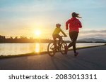 Small photo of Happy mother and son go in sports outdoors. Boy rides bike in helmets, mom runs on sunny day. Silhouette family at sunset. Fresh air. Health care, authenticity, sense of balance and calmness