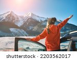 Woman traveling exploring, enjoying the view of the mountains, landscape, lifestyle concept winter vacation outdoors.Female standing near the car in sunny day, travel in the mountains, freedom.