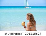 Portrait of young beautiful girl at tropical beach for vacations in Varadero, Cuba, drinking cocktail in coconut and sitting on sand