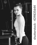 Small photo of Young slim woman doing pushdown on cable machine in gym. Athletic girl training triceps in fitness center. Black and white image.