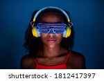 Young woman wearing headphones and futuristic led glasses on blue background - Isolated black woman wearing 3d smart glasses and headphones - virtual reality, future, technology concept 