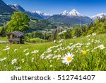 Beautiful view of idyllic mountain scenery in the Alps with traditional old mountain chalet and fresh green meadows with blooming flowers on a sunny day with blue sky in springtime