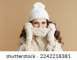 Hello winter. stylish middle aged woman in beige sweater, mittens and hat wrapped in a collar isolated on beige.