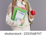 Closeup on teenager girl in beige tracksuit with apple, backpack, workbooks, headphones and textbook isolated on grey background.