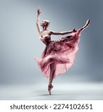 Small photo of Ballerina in Pink Chiffon Dress jumping Split. Ballet Dancer in Silk Gown Pointe Shoes. Graceful Woman in Tutu Skirt dancing over Gray Background