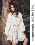Small photo of Outdoor fashion: portrait of the beautiful young boho (hippie) girl in grove (forest). Cute hippy woman stands at the tree at sunset time