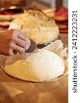 Small photo of Bread scoring. Close up vertical photo with a male hand scoring the sourdough bread before cooking the home made bread. Bakery at home. Wheat flour dough scoring. How to score the bread with a blade.