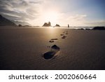 Footprints in sand against silhouette of person. Man walking along beach to sea at golden sunset. Tenerife, Canary Islands, Spain.