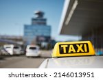 Selective focus on taxi sign on roof of car against airport terminal. 