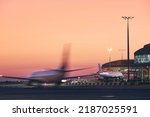 Airplane in blurred motion. Traffic at airport during colorful sunrise.