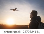 Man with backpack looking up to airplane landing at airport during beautiful sunset. 